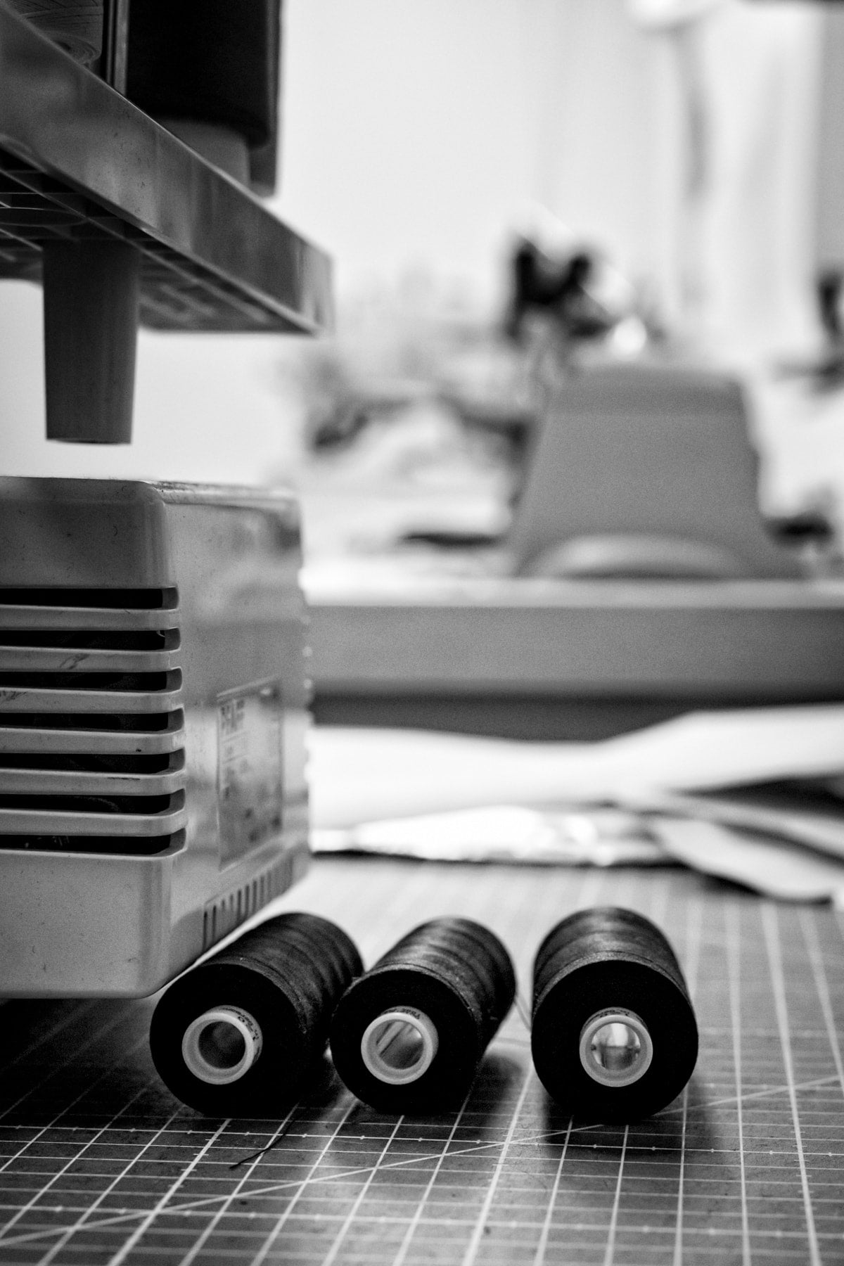 Mode-Atelier Detail: Schwarze Garnrollen vor Nähmaschine bei der Fertigung.